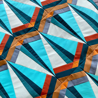 Close-up of a modern geometric quilt design featuring blue, teal, orange, and gray tones, created using the Skye FPP Quilt Pattern (Download) by Julia Wachs Designs.