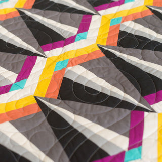 Close-up of a vibrant geometric quilt in gray, yellow, purple, teal, and orange tones, showcasing the Skye FPP Quilt Pattern (Download) by Julia Wachs Designs.