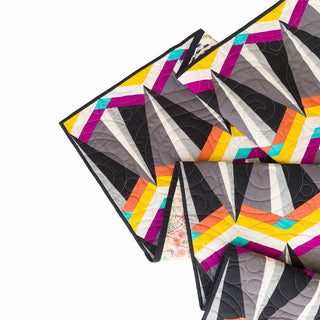 Close-up of a colorful modern quilt showcasing geometric shapes in bold yellow, purple, orange, teal, and gray hues, created with Skye FPP Quilt Pattern (Download) by Julia Wachs Designs.