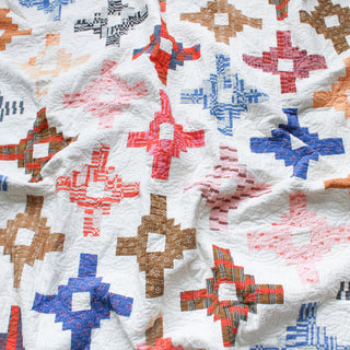 Close-up of a colorful quilt featuring geometric patterns on a white background, showcasing the Southwest Knit Quilt Pattern (Download) by Month of May Quilting.