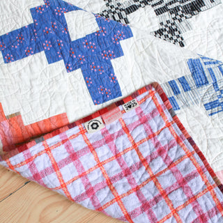 Close-up of a handmade quilt featuring geometric blue, black, and white knit patterns with a soft, colorful checkered backing, showcasing the Southwest Knit Quilt Pattern (Download) by Month of May Quilting.