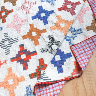 Close-up of a colorful geometric quilt with plaid and solid patterns featuring reds, blues, and oranges, showcasing Month of May Quilting’s Southwest Knit Quilt Pattern (Download).