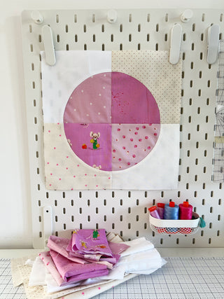 Spring Moon Quilt Pattern (Download) block in soft pinks and creams by Lou Orth Designs, displayed on a pegboard with coordinating fabric and sewing threads.