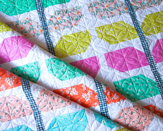 Closeup of a colorful quilt made with geometric shapes in bright floral fabrics and blue checkered sashing, showcasing Lou Orth Designs craftsmanship in the Sprout Quilt Pattern (Download).