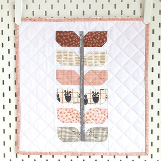 Small quilt block featuring a modern sprout design with earth tones and a gray stem, showcasing the Sprout Quilt Pattern (Download) by Lou Orth Designs.