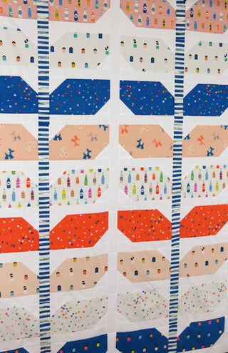 Close-up of a colorful quilt featuring various whimsical prints including bottles, stars, and balloons separated by striped sashing, showcasing the Sprout Quilt Pattern (Download) by Lou Orth Designs.