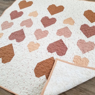 Quilt with heart-shaped patterns in various shades of brown and pink on a wooden surface.