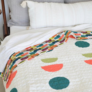 Close-up of a colorful quilt with geometric shapes draped over a bed, showcasing a modern design by Sewn from the Sunroom Quilt Pattern (Download).