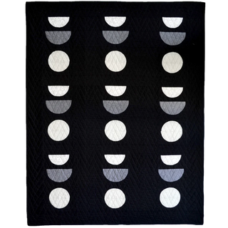 Sunroom Quilt Pattern by Sewn cover flat lay: black quilt with rows of curved half-circle blocks in white, grey, and navy creating a moon phase effect.