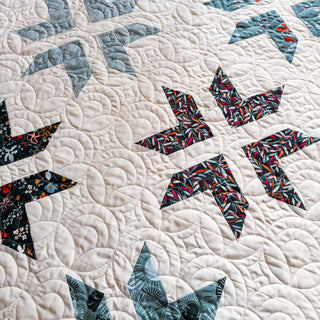 Close-up of a quilt featuring intricate star blocks with floral fabrics on a cream background, showcasing detailed stitching from A Piece of Quiet Quilts for the Super Star Quilt Pattern (Download).
