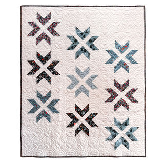 White quilt with a modern geometric star pattern in shades of blue and black, featuring intricate quilting details, showcasing the Super Star Quilt Pattern (Download) by A Piece of Quiet Quilts.