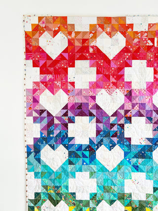 Close-up of a colorful quilt with heart and cross blocks in a gradient of warm to cool tones, showcasing detailed piecing from Lou Orth Designs Sweet Darlings Quilt Pattern (Download).