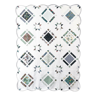 White quilt featuring floral and geometric blocks with a scalloped edge, showcasing the Timber & Glow Quilt Pattern (Download) by Sew & Sew Quilting Co.