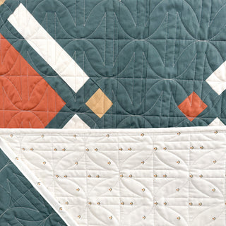 Close-up of a modern quilt showcasing geometric shapes and detailed stitching from the Timber & Glow Quilt Pattern (Download) by Sew & Sew Quilting Co.