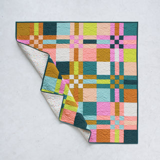 Colorful geometric quilt with interlocking squares in pink, teal, orange, and green, partially folded to show a patterned backing, showcasing the To The Nines Quilt Pattern (Download) by Patternly Collective.
