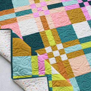 Colorful geometric quilt with intricate swirling stitch patterns displayed flat with one corner folded, showcasing the To The Nines Quilt Pattern (Download) by Patternly Collective.
