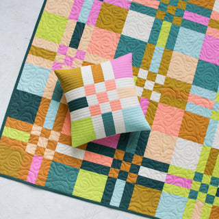 Colorful To The Nines quilt by Patternly with a matching pillow on a light background
