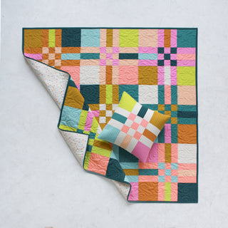Colorful geometric quilt and matching pillow made with modern blocks in green, pink, orange, and blue tones, showcasing the To The Nines Quilt Pattern (Download) by Patternly Collective.