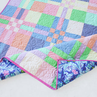 Close-up of a pastel geometric quilt with a floral backing, showcasing detailed quilting and binding, representing the To The Nines Quilt Pattern (Download) by Patternly Collective.