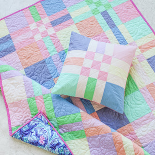 Pastel-colored quilt and matching pillow featuring geometric patterns with green, pink, purple, and blue shades, styled to showcase the To The Nines Quilt Pattern (Download) by Patternly Collective.
