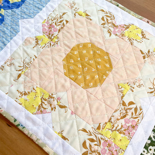Close-up of a quilt block featuring floral and geometric patterns in soft yellow, pink, and blue tones from Trula's Blooms Table Runner Quilt Pattern (Download) by Heart Lake Quilts