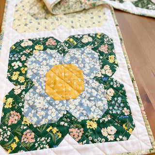 Close-up of a floral quilt block from Trula's Blooms Table Runner Quilt Pattern (Download) by Heart Lake Quilts featuring green, blue, and yellow fabrics with intricate stitching.