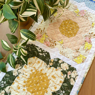 Close-up of a floral quilted table runner with warm yellow, pink, and green fabrics and geometric flower blocks, showcasing Trula's Blooms Table Runner Quilt Pattern (Download) by Heart Lake Quilts.