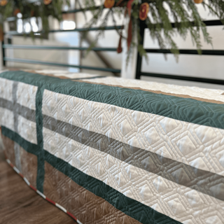 Close-up of a geometric quilt with green, beige, and gray tones, showcasing detailed stitching from Sew & Sew Quilting Co.'s Urban Pine Quilt Pattern (Download).