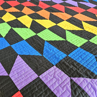 Vibrant Quilt Pattern by Staci W Quilts closeup: bold rainbow-colored triangular blocks on a black background in red, orange, yellow, green, blue, and purple.