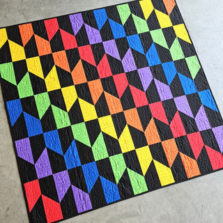 Colorful geometric quilt with repeating diamond and house-like shapes in rainbow hues on a black background, showcasing the Vibrant Quilt Pattern (Download) by Staci W Quilts.
