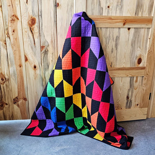 Colorful geometric quilt with vibrant red, orange, yellow, green, blue, and purple blocks accented by black, showcased by Staci W Quilts, featuring Vibrant Quilt Pattern (Download).