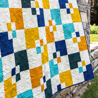 Colorful Welcome Party quilt by Trace Creek Quilting with geometric pattern draped over a stone surface