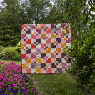 Welcome Party quilt by Trace Creek Quilting displayed outdoors with greenery and flowers in the background