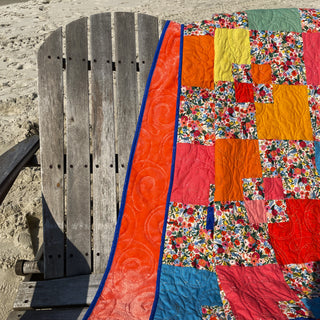 Colorful Welcome Party quilt by Trace Creek Quilting draped over a wooden chair on a sandy background
