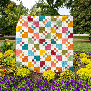 Welcome Party quilt by Trace Creek Quilting displayed outdoors with greenery and flowers in the background