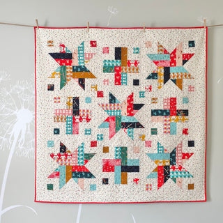 Colorful patchwork quilt with star and geometric blocks hanging on a wall, made using the Wink Quilt Pattern (Download) by The Dandy Patch.