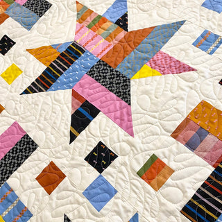 Close-up of a colorful geometric quilt with star and square shapes in blues, pinks, yellows, and oranges, showcasing intricate stitching from The Dandy Patch using Wink Quilt Pattern (Download).
