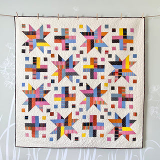Wink quilt pattern by The Dandy Patch: colorful star-patterned quilt hanging on a line against a light background