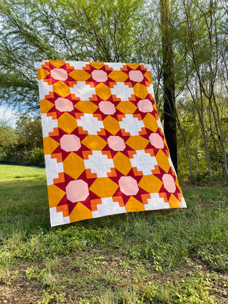 Colorful geometric quilt on grass with trees in the background