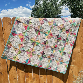 Amazing Grace Quilt Pattern (Download) by The Gluten Free Quilter featuring a pastel geometric quilt with interlocking diamonds and colorful pinwheels draped over a wooden fence