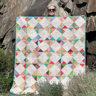 Amazing Grace Quilt Pattern (Download) by The Gluten Free Quilter featuring a colorful geometric quilt with interlocking diamonds and rhythmic pinwheels outdoors