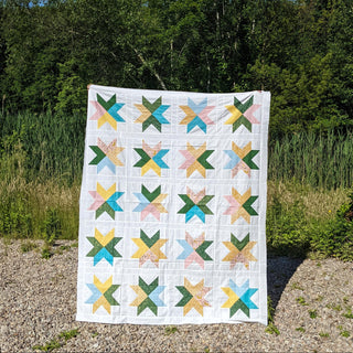 Beaming Quilt Pattern (Download) by Homemade Emily Jane featuring a bright modern star quilt with colorful geometric blocks displayed outdoors
