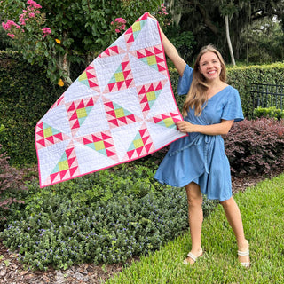 Brazen Quilt Pattern (Download) by Homemade Emily Jane showing a woman holding a colorful modern geometric quilt with pink green and blue triangles outdoors