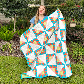 Smiling woman displays a colorful geometric quilt outdoors for Brazen Quilt Pattern (Download) by Homemade Emily Jane