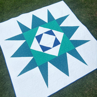 Catalyst Quilt Pattern (Download) by Homemade Emily Jane featuring a bold teal and blue geometric star design on white fabric outdoors