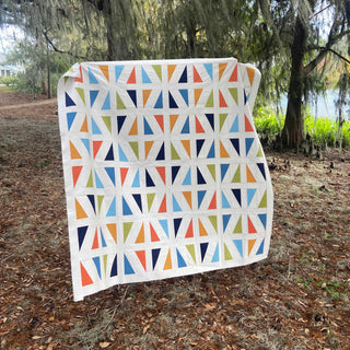 Jubilant Quilt Pattern (Download) by Homemade Emily Jane featuring a colorful modern quilt with bold geometric triangles and creative negative space outdoors