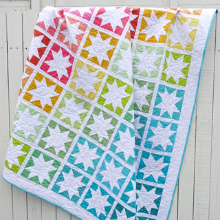 Keepsake Quilt Pattern (Download) by Homemade Emily Jane featuring a colorful modern star quilt with white stars and rainbow geometric blocks draped on a wall