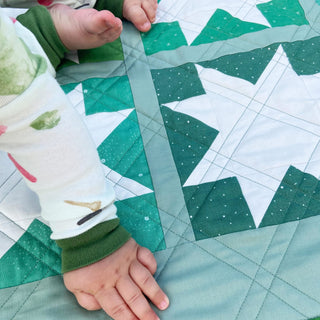 Keepsake Quilt Pattern (Download) by Homemade Emily Jane showing a modern teal and white Sawtooth Star quilt with child hands