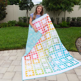 Keepsake Quilt Pattern (Download) by Homemade Emily Jane showing a colorful modern star quilt with pastel blocks held outdoors by a smiling woman