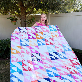 Kinetic Quilt Pattern (Download) by Homemade Emily Jane featuring a colorful modern geometric quilt with pink blue and white patchwork triangles outdoors